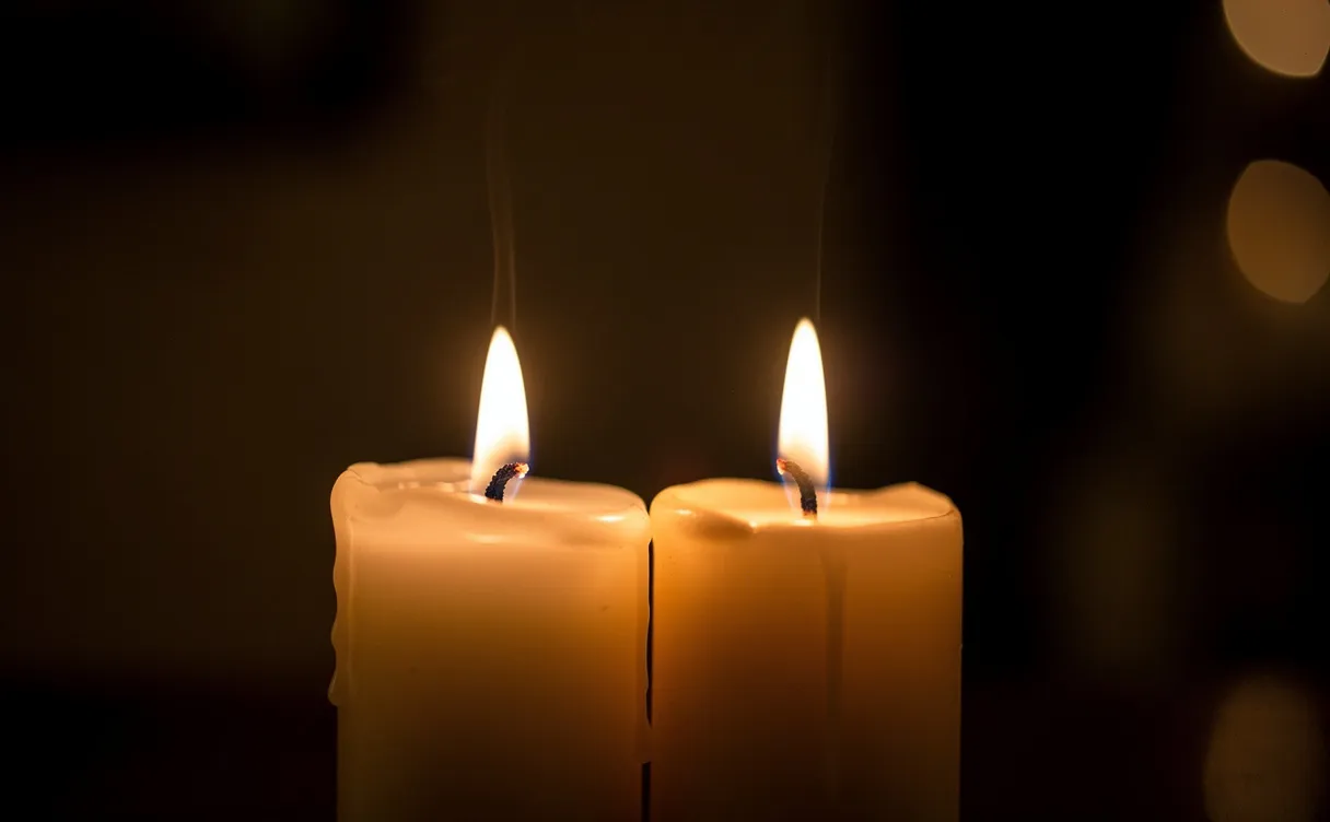 Deux bougies allumées côte à côte diffusent une lumière chaleureuse sur un fond sombre.
