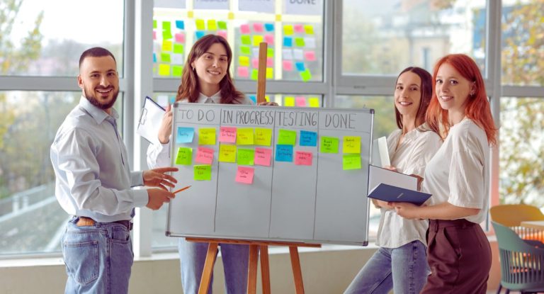 Equipe projet souriante devant un tableau kanban avec colonnes a faire en cours termine